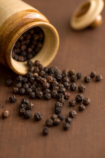 Close up of black pepper or peppercorns with clay pot