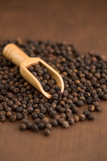 Close up of black pepper or peppercorns in wood scoop