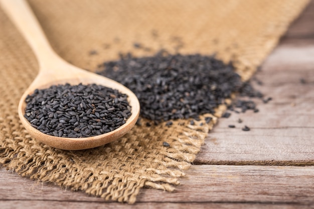 Close up black sesame in bowl and spoon on wooden plank background