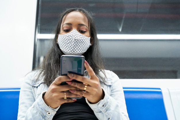 Chiuda in su della donna nera seduta da sola nel vagone della metropolitana utilizzando uno smartphone.