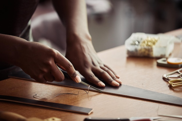 Primo piano di una giovane donna nera che taglia la pelle e crea una cintura fatta a mano nello spazio della copia dell'officina