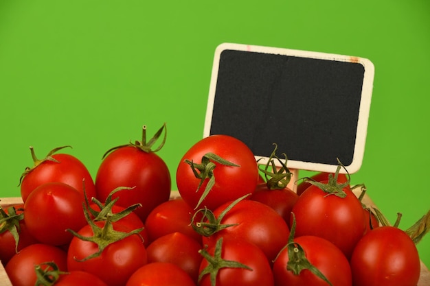 Photo close-up of blank chalkboard with fresh cherry tomatoes against green background