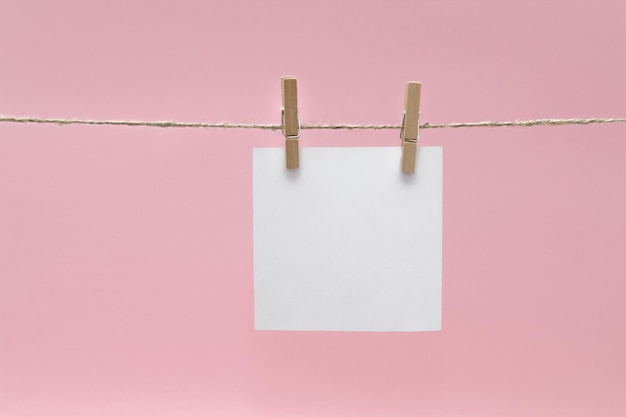 Photo close-up of blank notes hanging on rope against pink background