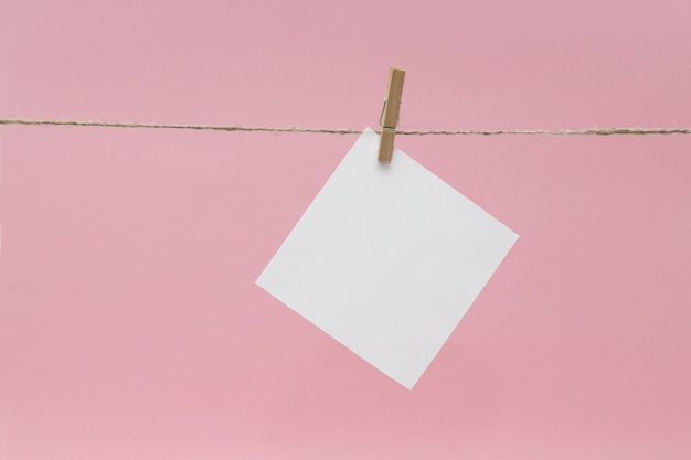 Photo close-up of blank notes hanging on rope against pink background