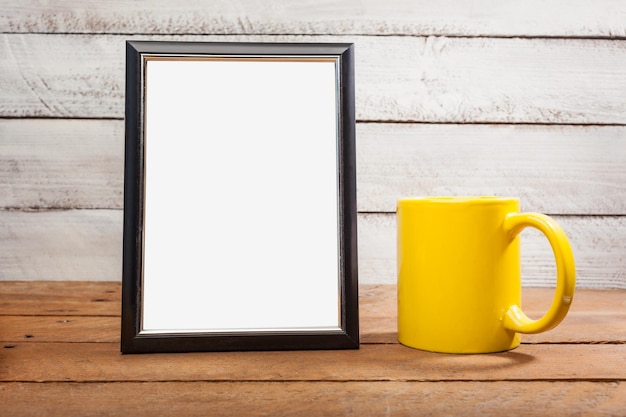 close-up of blank picture frame with coffee cup on wooden table against wall