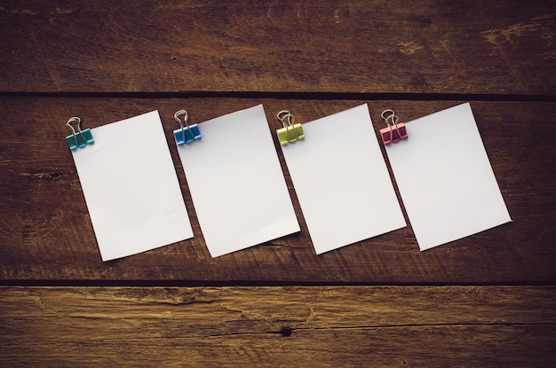 Photo close-up of blank white papers with binder clips on wooden table