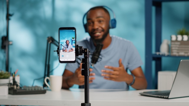 Close up of blogger filming video with smartphone on tripod for online vlog. Content creator using mobile phone and videography equipment to record for podcast channel on social media.