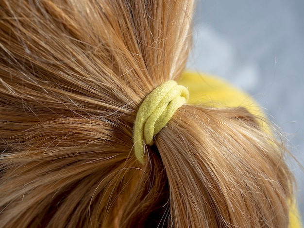 Close up of blonde hair tied in a bun with a yellow elastic band