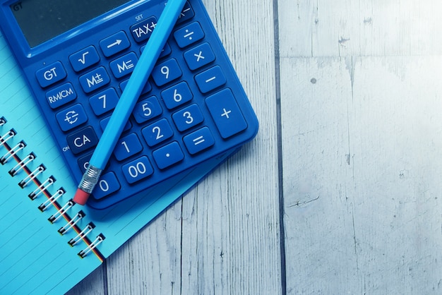 Close up of blue calculator and notepad on color background