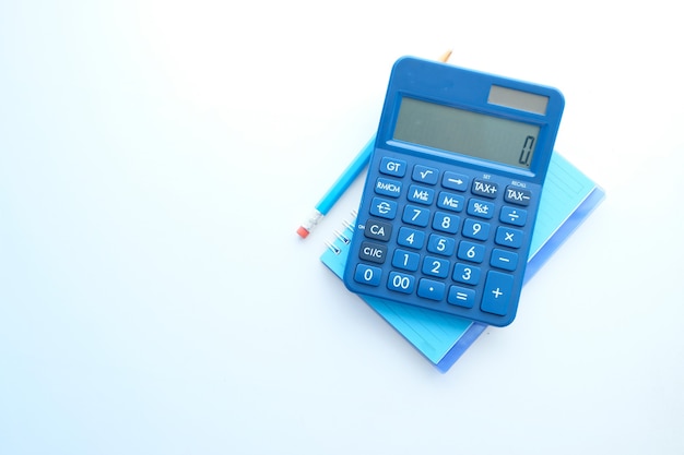 Close up of blue calculator and notepad on white table .