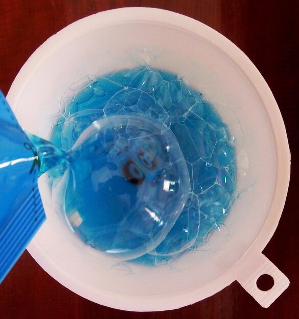 Photo close-up of blue dishwashing liquid being poured in funnel