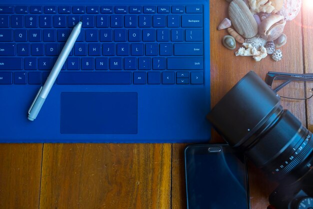 Close-up of blue laptop with smart phone by eyeglasses and seashells on table