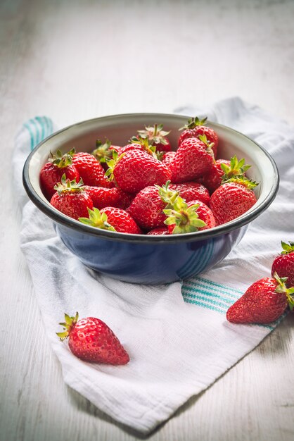 Close up of a blue metal bowl full of fresh strawberries over a white wood rustic ,