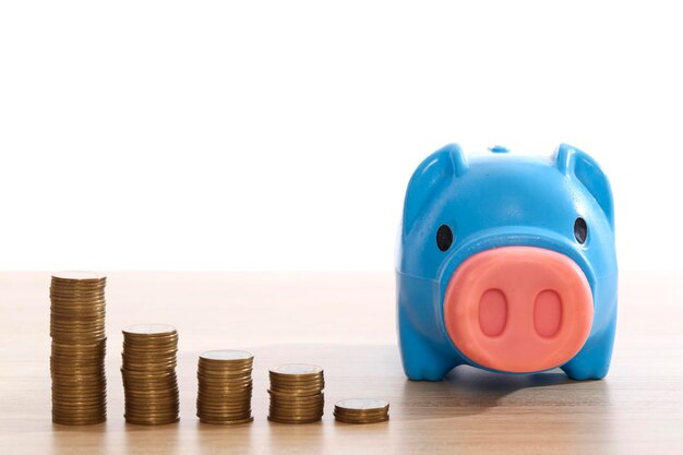 Photo close-up of blue piggy bank with coins on table against white background