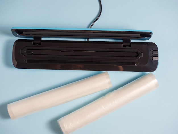 Close-up of a blue vacuum packer on a bright blue background. Next to the packaging bags. A machine for preserving the freshness of products. Flat lay, top view.