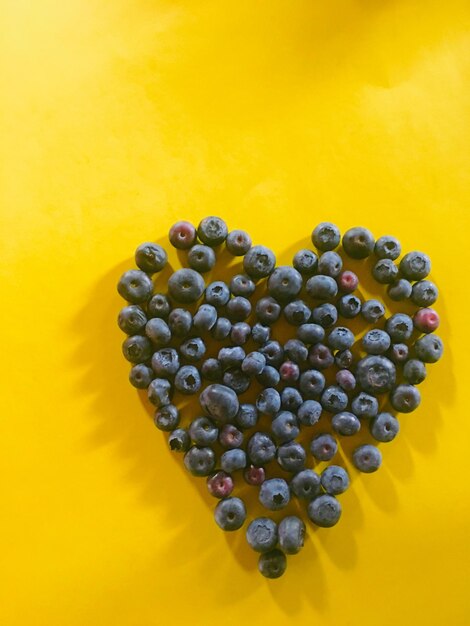 Close-up of blueberries in a heart shape against yellow background