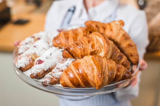 Close-up of blurred female baker holding fresh croissant in the tray