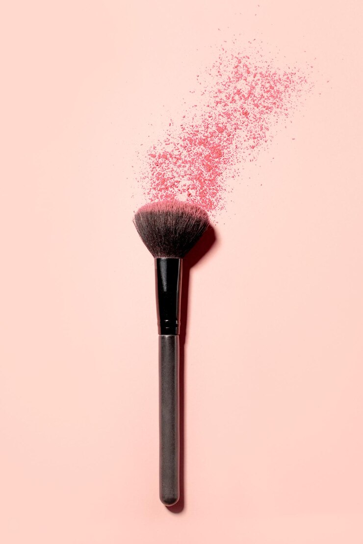Close-up on a blush brush with pink blush crumbling on top on a pink background