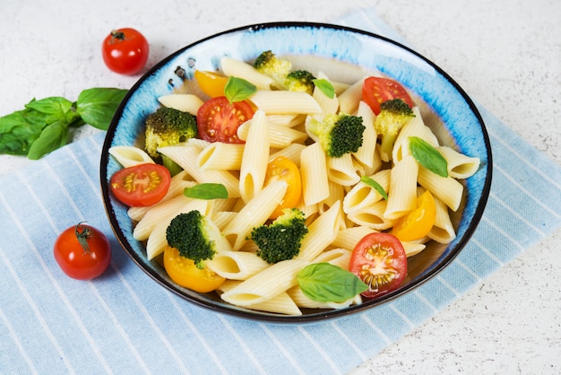 Primo piano di penne bollite con verdure, broccoli, pomodori ed erbe fresche.