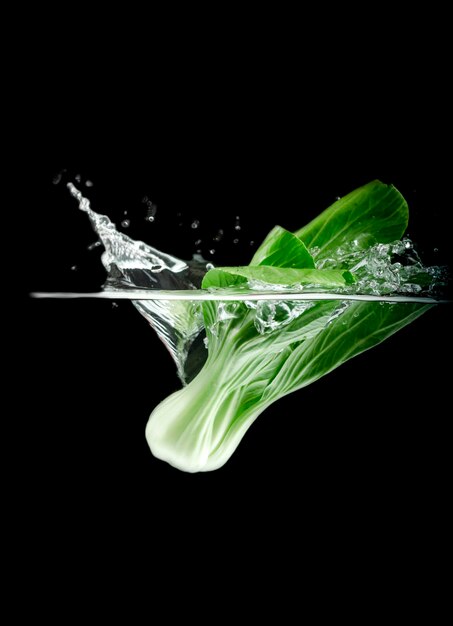 Foto close-up di bok choy che cade in acqua contro uno sfondo nero