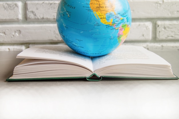 Foto primo piano di un libro aperto su una biblioteca libri da tavolo e un globo, contro un muro di mattoni in classe, la luce del sole, il concetto di giornata mondiale del libro