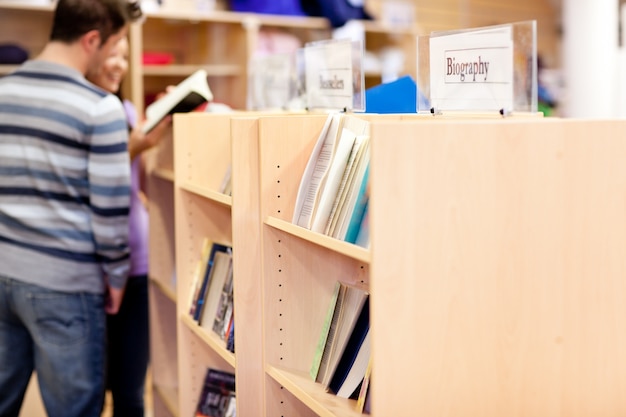 крупным планом книжных полок в библиотеке со студентами, читающими книгу