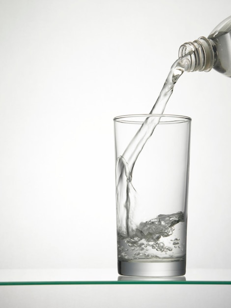 Photo close-up of bottle pouring water in glass against white background