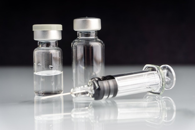 Close-up of bottles and syringe on table against black background