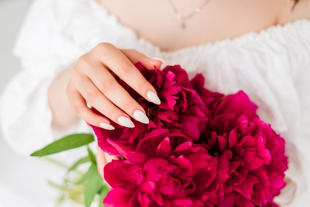 Close-up of a bouquet of peonies in the hands of a girl. Girl in white dress holding red flowers