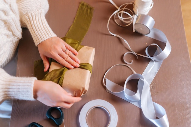 Close-up bovenaanzicht van onherkenbare jonge vrouw die lint vastbindt op ingepakte kerstcadeaudoos met cadeautjes voor familie en vrienden