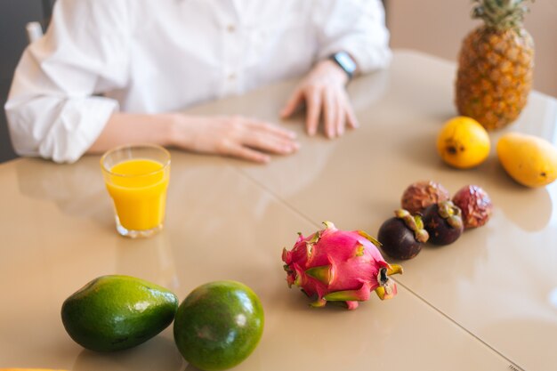 Close-up bovenaanzicht van onherkenbare jonge vrouw zittend aan houten tafel met exotisch tropisch fruit in