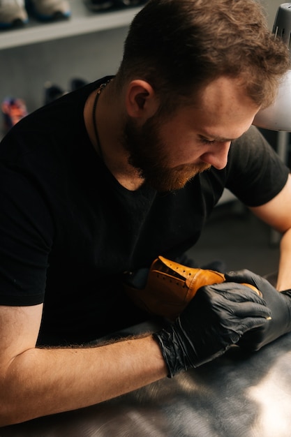 Close-up bovenaanzicht van schoenmaker die zwarte latexhandschoenen draagt die oude lichtbruine leren schoenen met...