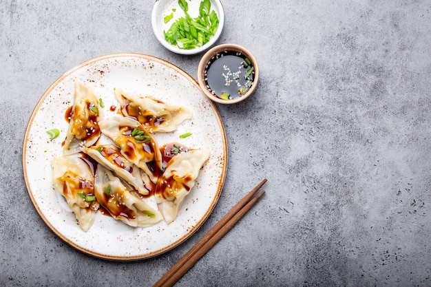 Close-up, bovenaanzicht van traditionele Aziatische/Chinese dumplings op wit bord met sojasaus en eetstokjes op grijze rustieke stenen achtergrond met ruimte voor tekst. Authentieke Chinese keuken, kopieer ruimte