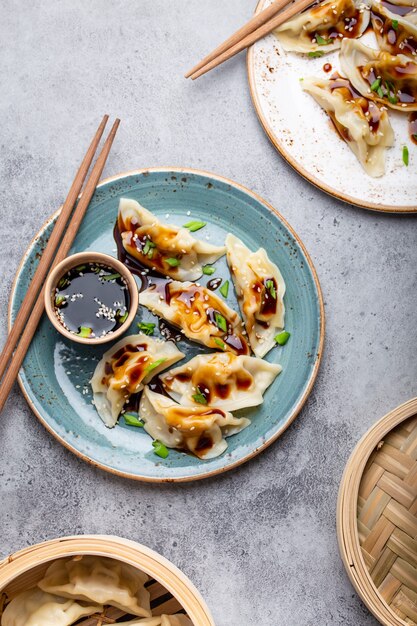 Close-up, bovenaanzicht van twee platen met traditionele Aziatische/Chinese dumplings met sojasaus en eetstokjes op grijze rustieke stenen achtergrond. Authentieke Chinese keuken