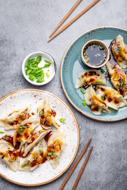 Close-up, bovenaanzicht van twee platen met traditionele Aziatische/Chinese dumplings met sojasaus en eetstokjes op grijze rustieke stenen achtergrond. Authentieke Chinese keuken