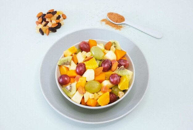 Крупный план на миске, наполненной свежим и красочным фруктовым салатом, апельсиновым фруктом, киви, папайей, дыней, яблоком, миндалем, коричневым сахаром на ложке