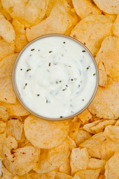 Photo close up of a bowl of white dip surrounded by nachos