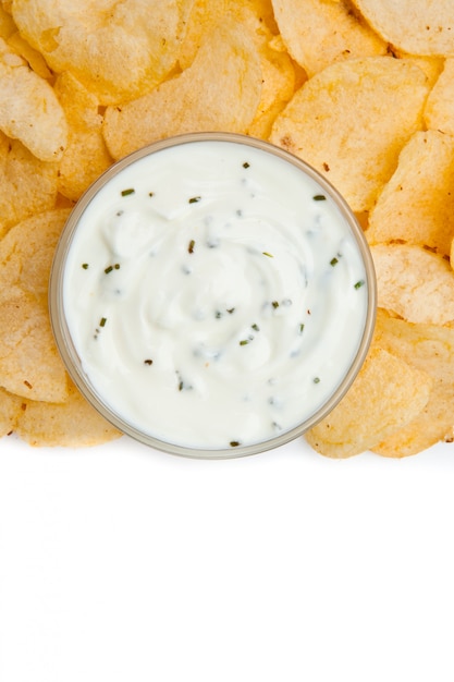 Photo close up of a bowl of white dip with herbs surrounded by nachos