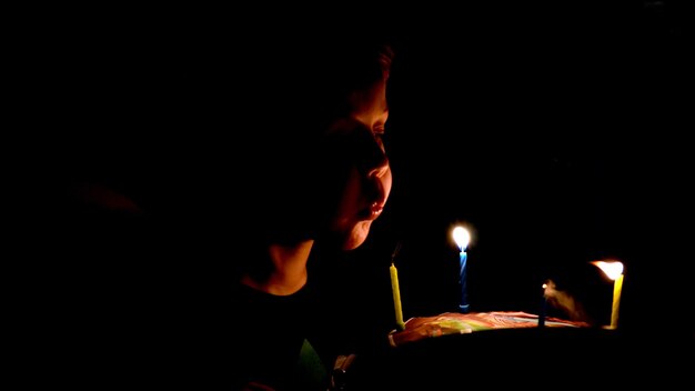Foto close-up di un ragazzo che soffia candele di compleanno su una torta al buio