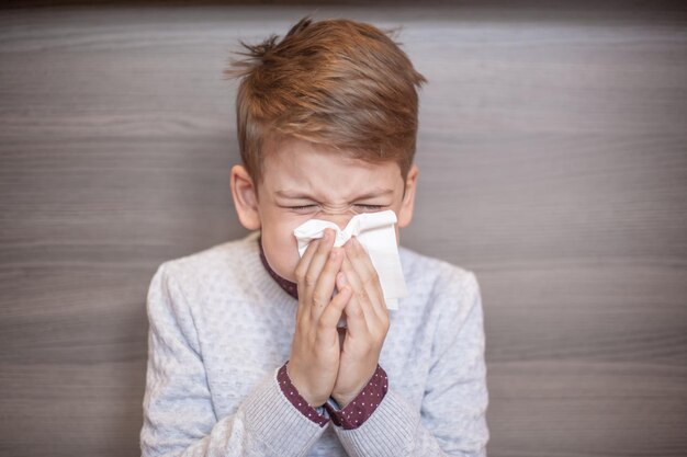 Photo close-up of boy blowing nose while sitting at home