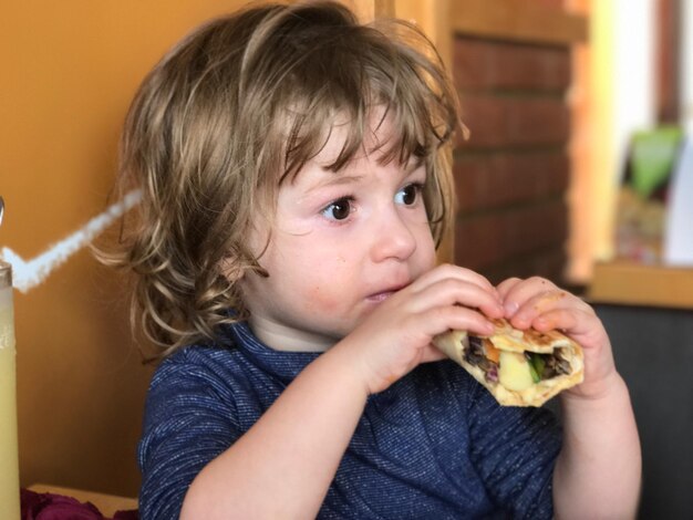 Foto close-up di un ragazzo che mangia un panino a casa