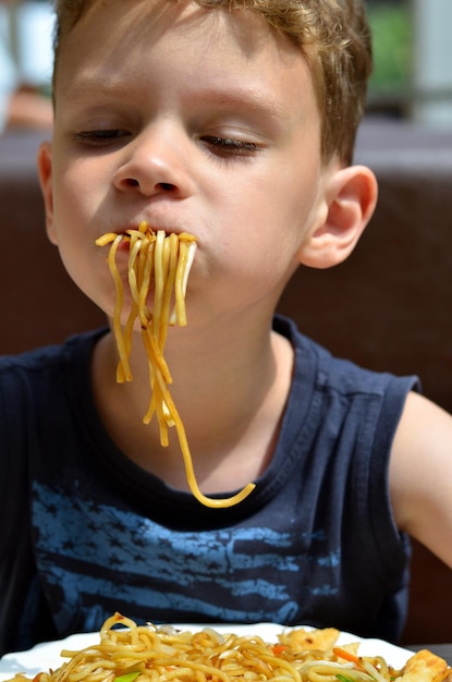 Photo close-up of boy eating spaghetti at restaurant