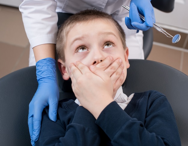 Il primo piano del ragazzo spaventato dai dentisti si copre la bocca e lo cerca