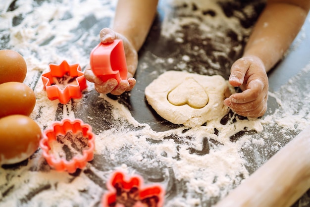 Close up of boy hands carving dough with cookie heart cutters Easter baking preparation