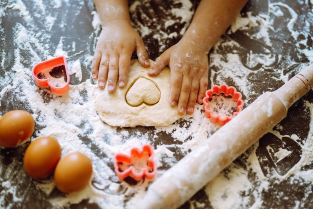 Close up of boy hands carving dough with cookie heart cutters Easter baking preparation