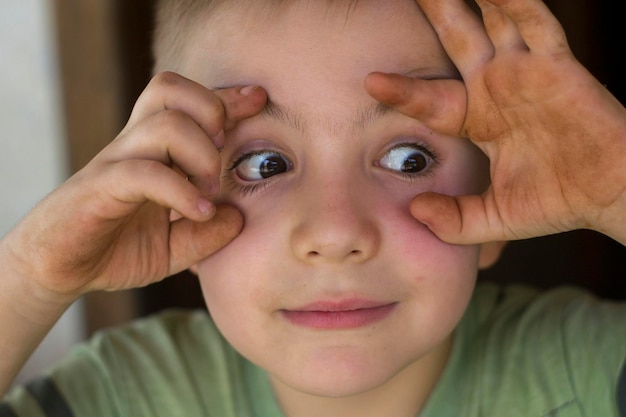 家で手で目を開ける男の子のクローズアップ