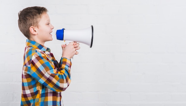 Close-up of a boy shouting loudly in megaphone against white background