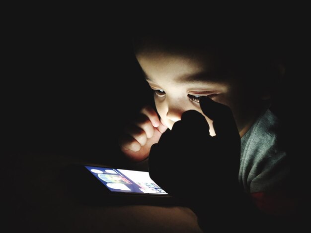 Photo close-up of boy using smart phone in darkroom