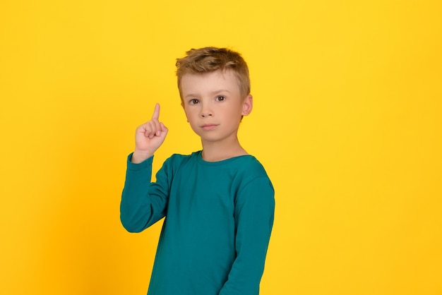 Close-up of a boy with a serious expression showing his index finger up, an idea. Yellow background.