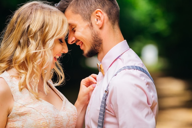 A close-up of a boyfriend who smiles and a girlfriend who fixes a wooden bow tie